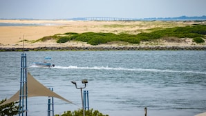 A beach with a boat on the water, a bridge in the background, and a rocky shoreline with greenery. - Walk to everything the inlet has to offer! Amazing bay views! (Ocean City)