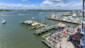 A marina with docks and boats, a pier with seating and umbrellas, and a distant shoreline with buildings. - Walk to everything the inlet has to offer! Amazing bay views! (Ocean City)