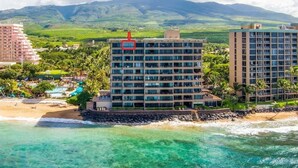 A beachfront hotel with multiple floors, a pool area, and a view of the ocean and mountains.