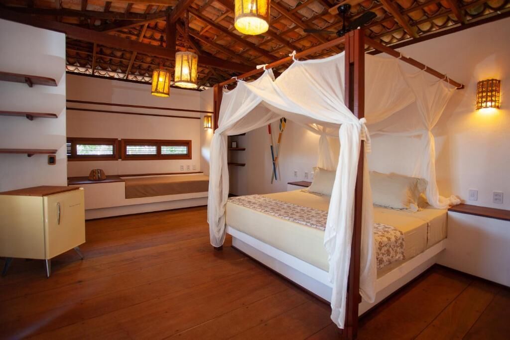 Un dormitorio con cama con dosel, suelo de madera, una mesita de noche y luces fijadas a la pared.