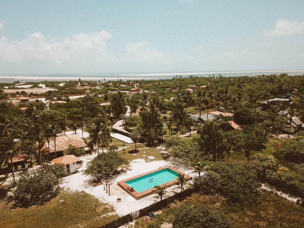 Vista aérea de un complejo turístico con piscina rodeada de vegetación y una playa al fondo.