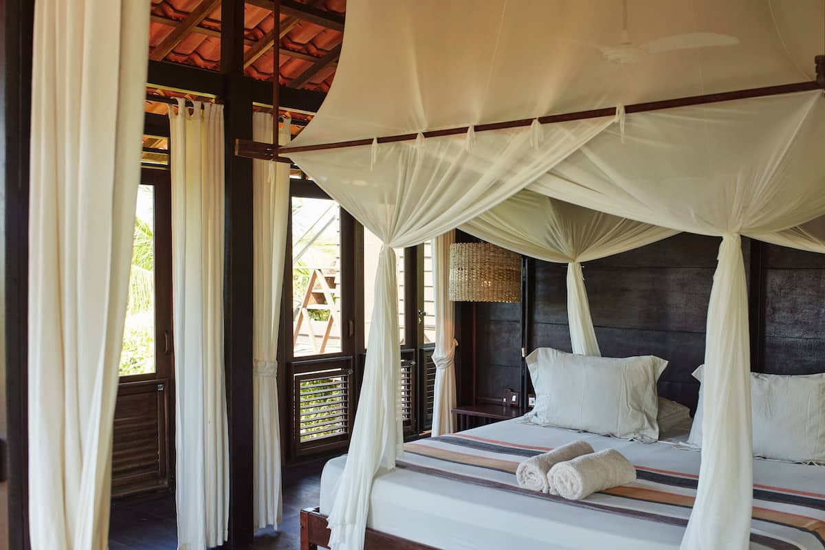 Una habitación con una cama, cortinas blancas y un dosel.