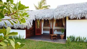 A thatched-roof bungalow with a wooden deck, a small seating area, and a potted plant.