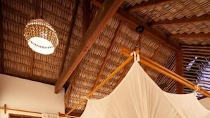 Een kamer met een bed onder een baldakijn, houten vloeren en een rieten plafond.