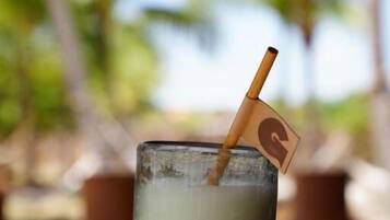 A hand holding a cocktail glass with a straw and a small flag, set against a blurred outdoor background.