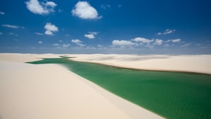 Een uitgestrekt woestijnlandschap met een helderblauwe lucht en een smalle waterloop erdoorheen.