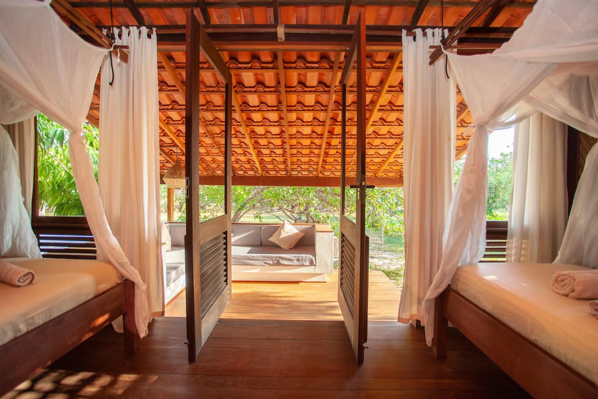 Una habitación con dos camas de madera, techo de madera y vista al verdor exterior.