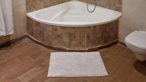 A bathroom with a corner bathtub, tiled walls, a toilet, and a white rug.