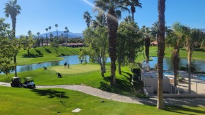 Un campo da golf con uno stagno, palme e una club house.