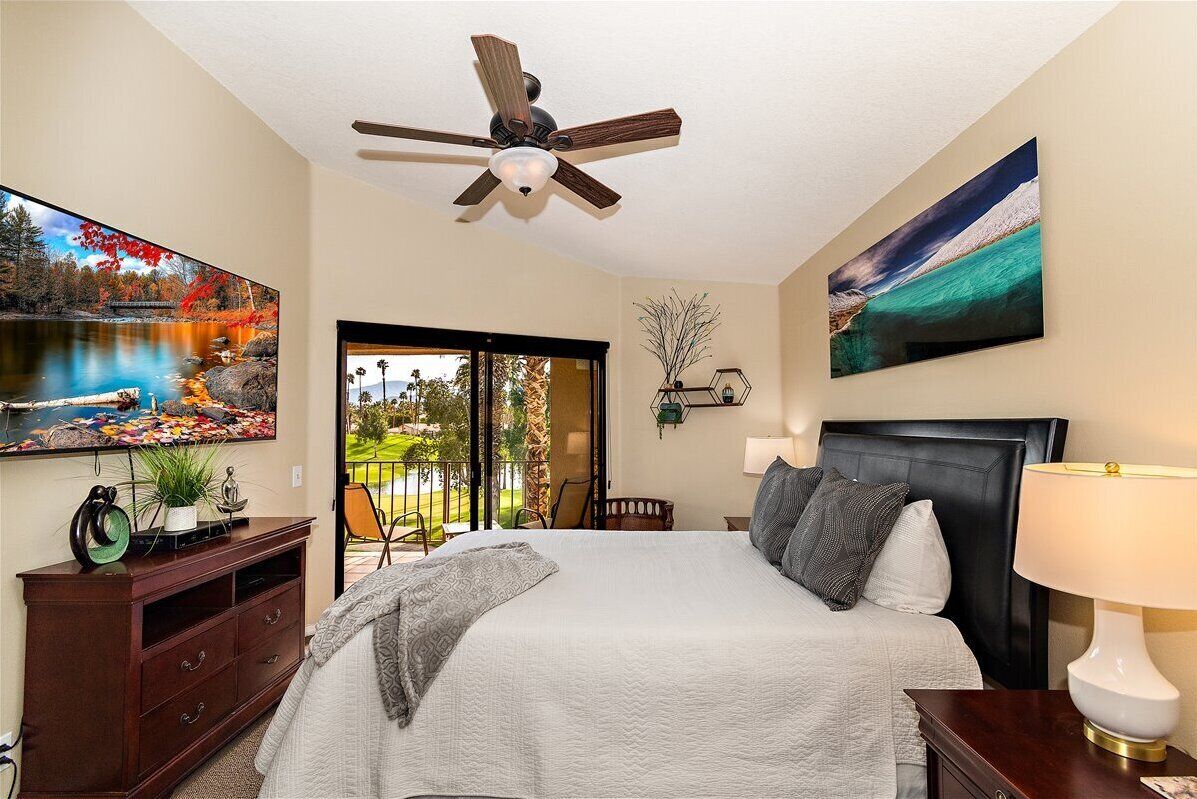 A bedroom with a bed, a ceiling fan, a TV, and artwork on the walls.