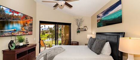 A bedroom with a bed, a ceiling fan, a TV, and artwork on the walls.