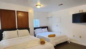 Un dormitorio con dos camas, una lámpara en el techo, un televisor y una ventana.