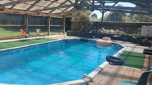 A rectangular swimming pool with a wooden deck surrounding it. There are four lounge chairs and a small inflatable pool in the corner. -  Captivating rural beauty, serene getaway, nestled midway  Rotorua & Taupo. (Rerewhakaaitu)