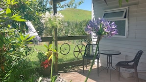 A patio with a table and chairs, surrounded by plants and a view of a hill. -  Captivating rural beauty, serene getaway, nestled midway  Rotorua & Taupo. (Rerewhakaaitu)