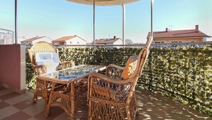 Un espacio de estar al aire libre cubierto con mobiliario de mimbre y una mesa de vidrio, con vistas a un barrio residencial.