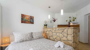 A bedroom with a stone accent wall, a bed with patterned bedding, a painting on the wall, and a nightstand with a lamp. - Holiday apartment with air conditioning (Labin)