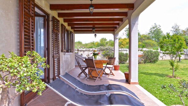 A covered outdoor area with a table and chairs, a bench, and a potted plant.