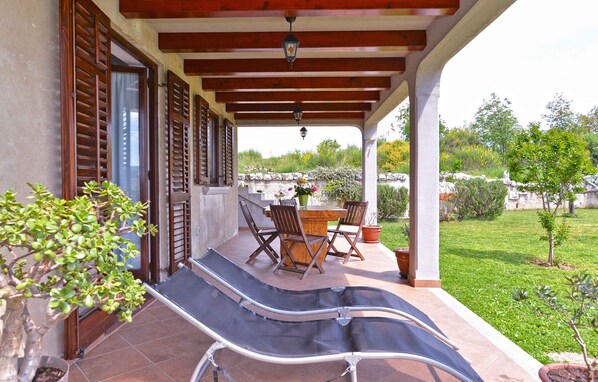 A covered outdoor area with a table and chairs, a bench, and a potted plant.