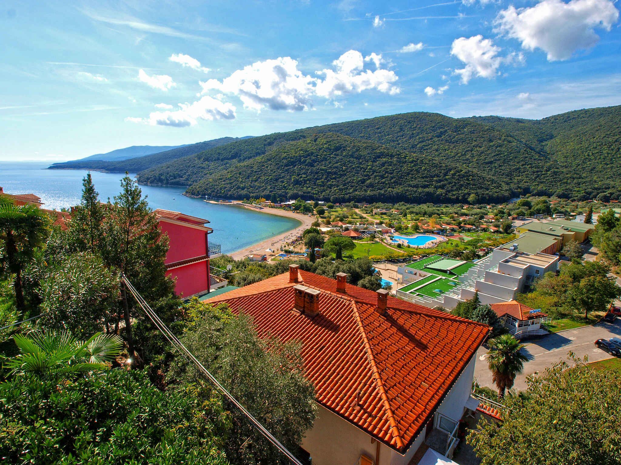 A coastal town with a beach, green hills, and a clear sky.