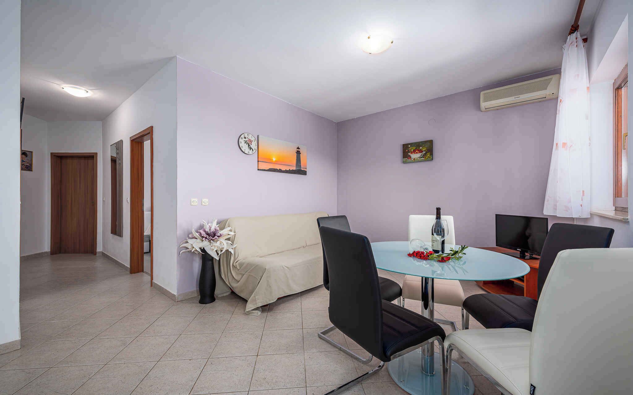 Un salon moderne avec une table ronde en verre, des chaises noires et blanches, un canapé, une horloge et un tableau représentant un coucher de soleil.