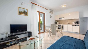 A modern living room with a TV, glass coffee table, and blue sofa. Adjacent is a kitchen with a fridge, microwave, and dining area. - Holiday apartment with air conditioning (Labin)