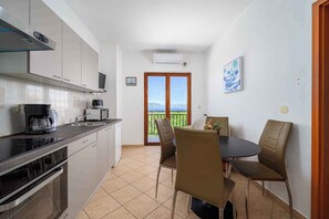 Une cuisine compacte dotée d’appareils électroménagers modernes, un coin repas avec deux chaises et une vue à travers une porte vitrée.