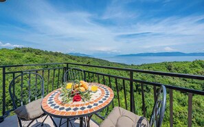 A round table with a mosaic tile design, surrounded by metal chairs, set on a balcony overlooking a lush green landscape and a body of water. - Holiday flat with air conditioning (Labin)