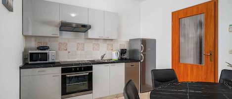 A compact kitchen with a microwave, stove, oven, and dishwasher. There's a wooden door and a dining table with chairs.