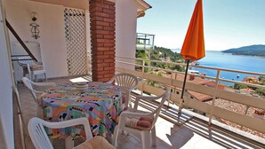 A balcony with a table and chairs, a view of the sea, and a brick pillar.