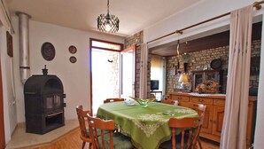A dining area with a wooden table and chairs, a stone fireplace, and a kitchen visible through an open doorway.