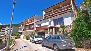 A multi-story residential building with balconies, a paved driveway, and parked cars.