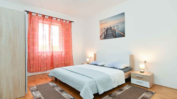 Une chambre à coucher avec un lit, des tables de chevet, un tableau et une fenêtre avec des rideaux.