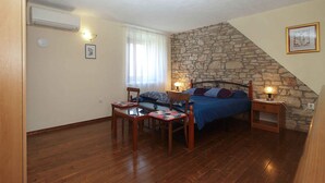 Un dormitorio con pared de piedra, cama con ropa de cama azul, mesa de madera con sillas y ventana con cortinas.