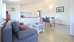 A modern living room with a grey sofa, a small white table, and a dining area with a table and chairs.
