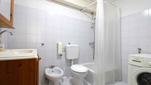 A bathroom with a sink, bidet, toilet, bathtub, and a washing machine. - Holiday apartment with balcony (Valbandon)