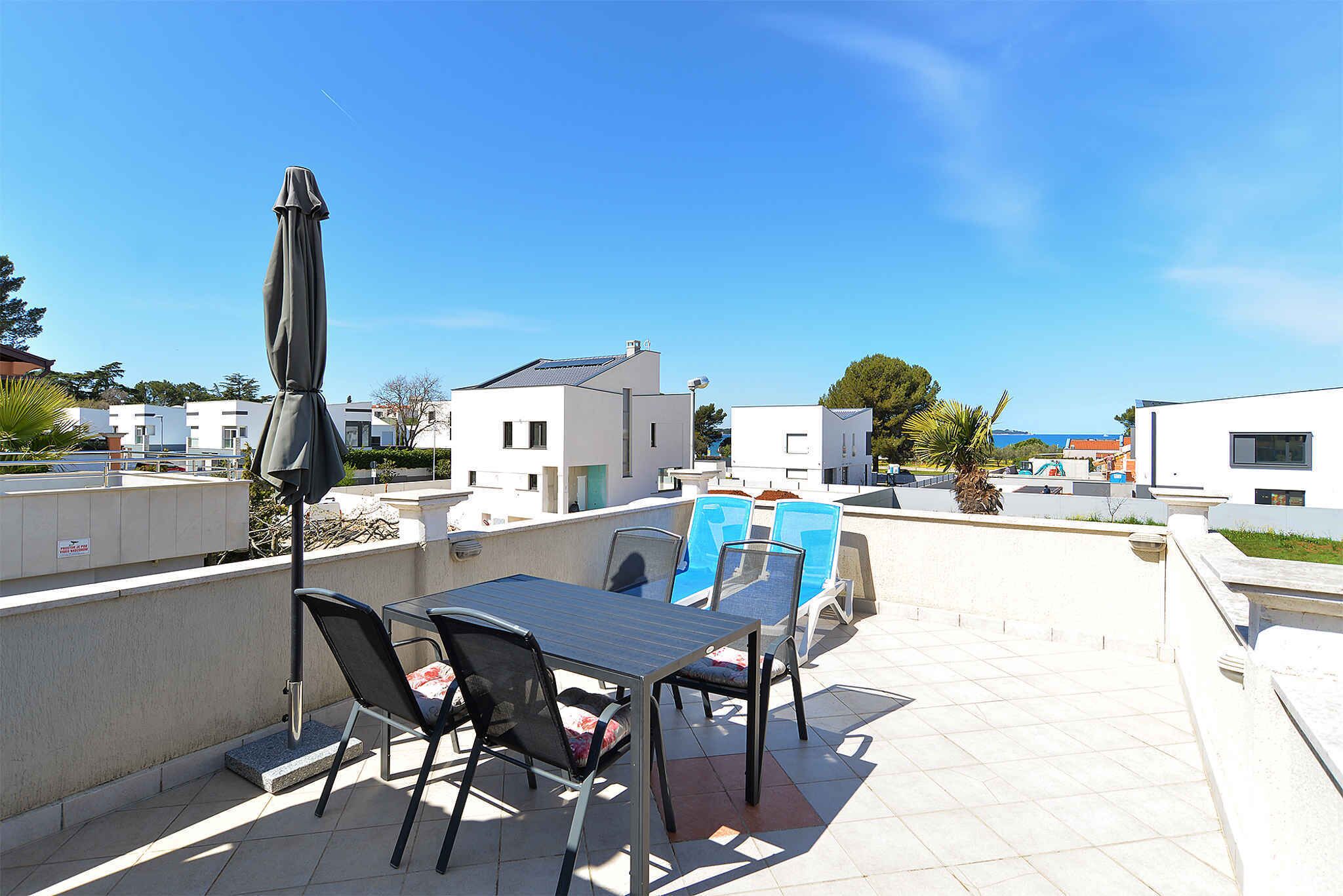 Eine Dachterrasse mit Tisch und Stühlen, einem Sonnenschirm und Blick auf die umliegenden Gebäude.