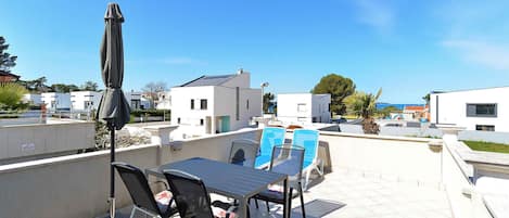A rooftop terrace with a table and chairs, a covered umbrella, and a view of surrounding buildings.