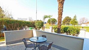 An outdoor patio with a round table and four chairs, surrounded by a low wall and various plants. - Holiday apartment with air conditioning (Fažana)