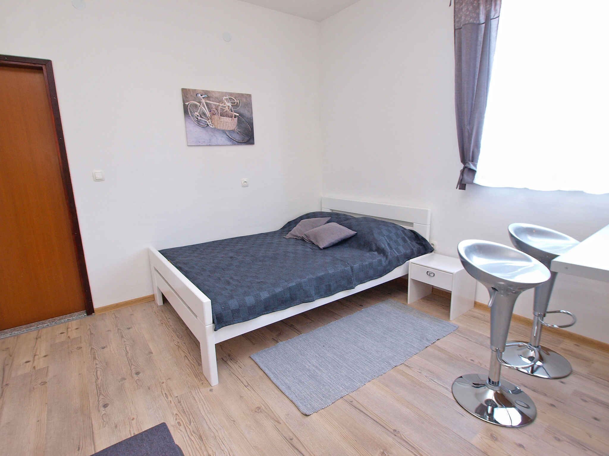 A small, neatly arranged bedroom with a single bed, a bedside table, a chair, and a small table.