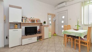 A compact living space with a TV, bookshelf, and dining area. - Holiday apartment with air conditioning (Pula)