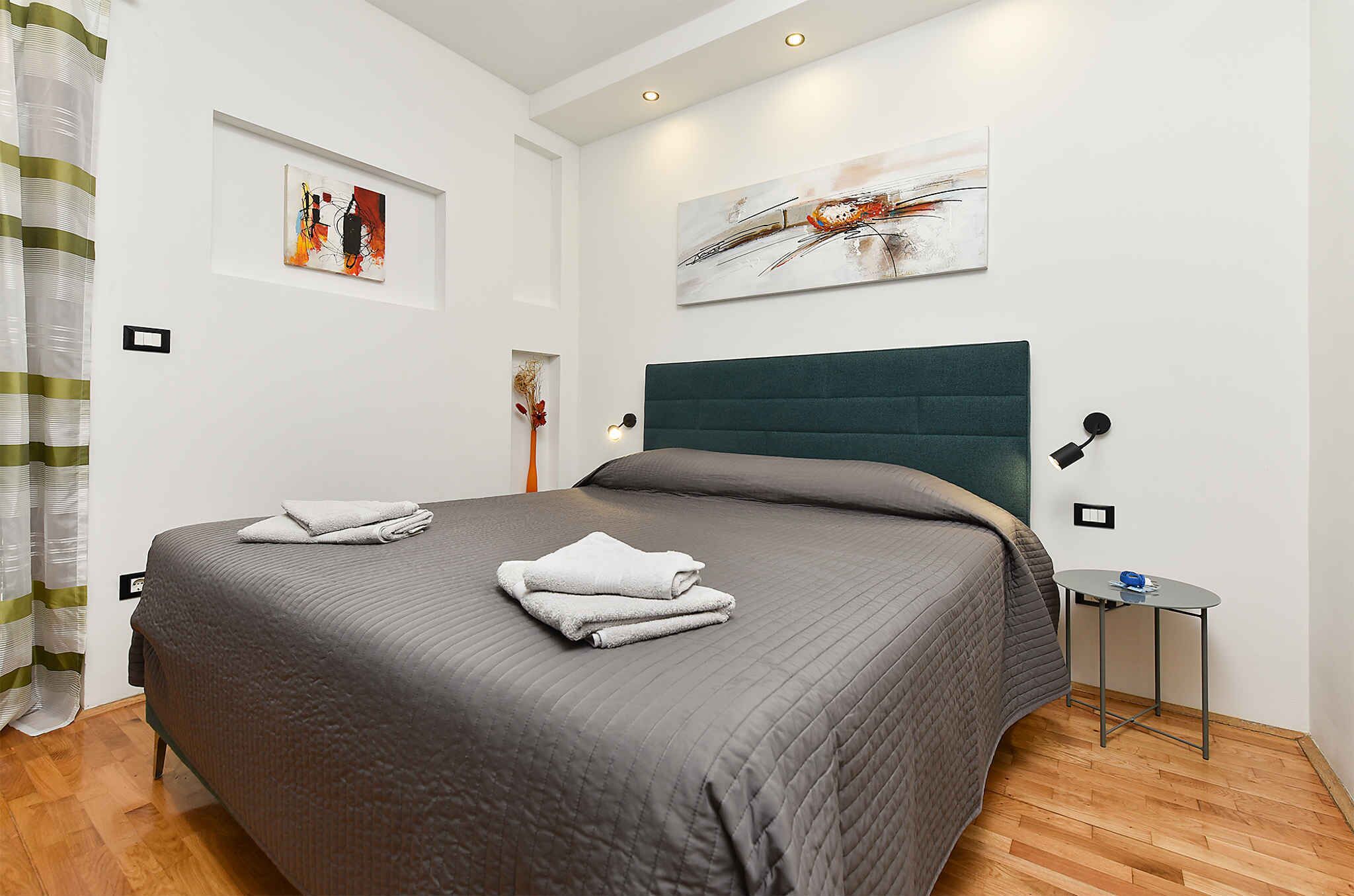 A neatly made bed with a dark headboard, a small bedside table with a lamp, and artwork on the walls.