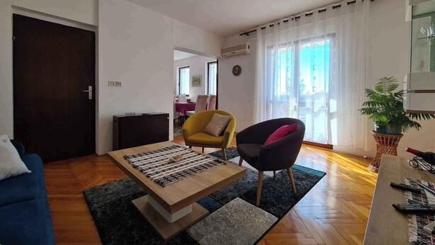 A living room with a sofa, a coffee table, a yellow armchair, a black armchair, and a potted plant.