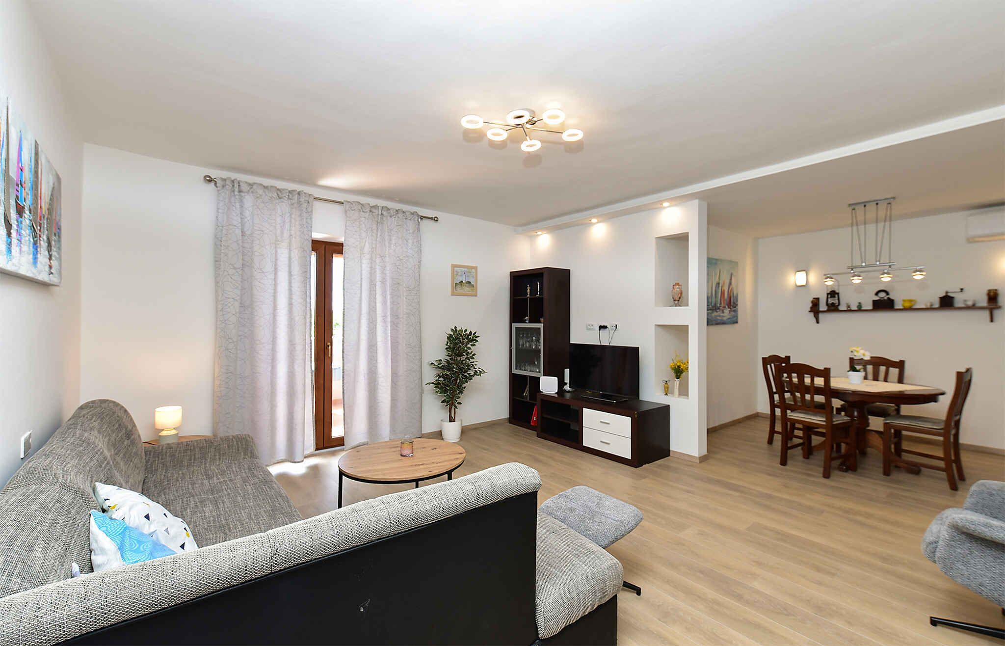 A living room with a sofa, a small round table, a TV stand, and a dining area with a table and chairs.