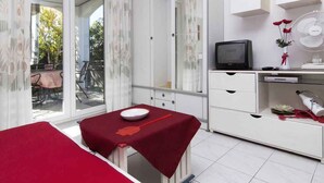 A room with a bed, a small table with a red tablecloth, a television, a fan, and a window with curtains. - Studio with terrace and air conditioning (Valbandon)