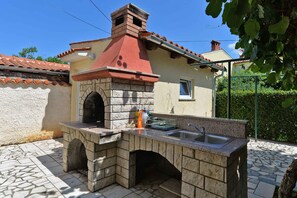 Una zona de cocina exterior con encimera de piedra, pileta e chimenea.