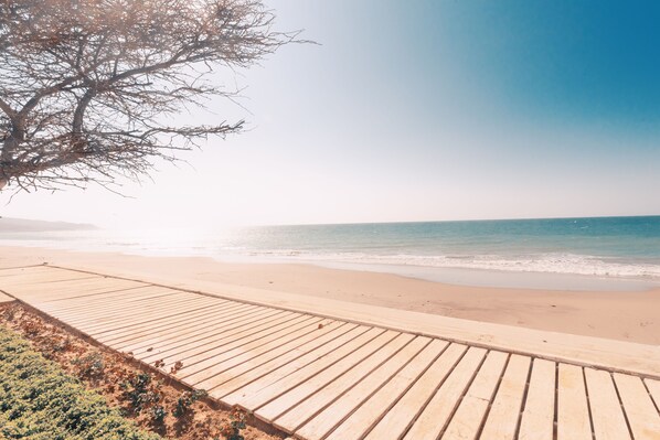 Un muelle de madera que conduce a una playa con cielos despejados y aguas tranquilas.
