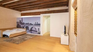 A bedroom with a bed, a large wall mural of a bridge, wooden beams, and a white bedside table with a TV.