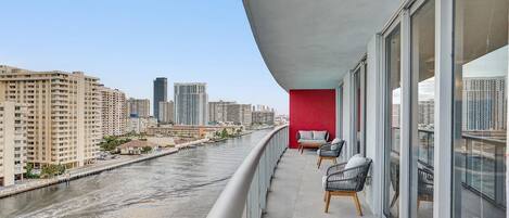 A balcony with two chairs, a red wall, and a view of a river and cityscape.