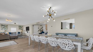 Un salón amplio con mesa de comedor, sillas blancas y un candelabro moderno.