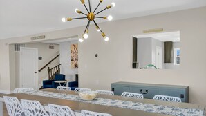 Un comedor con una mesa larga, sillas blancas, un sofá azul y una escalera que sube a otra habitación.